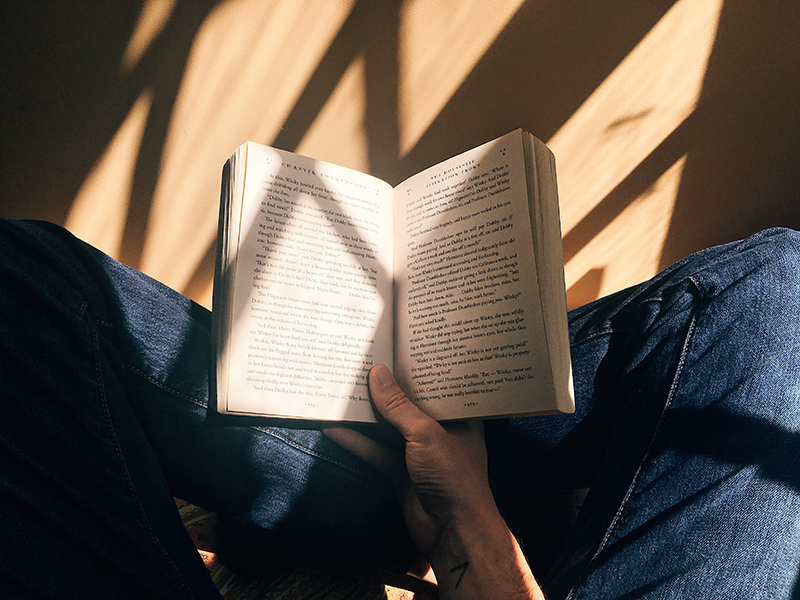 Person holding an open book with sunlight filtering in front windows and splaying over the pages