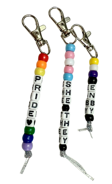 Three beaded keychains. The first one says Pride, the second says She They and the third says Enby.